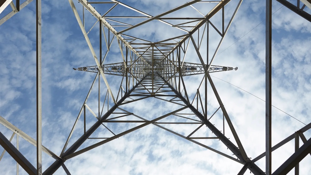 View from below through a power tower into the blue sky with white clouds.