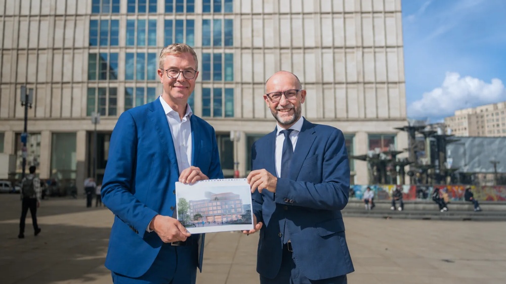 hausInvest-Fondsmanager Mario Schüttauf und Berlins Kultursenator Stefan Evers halten eine Visualisierung vor dem Alexanderplatz – Teaser zum Meilenstein am Alex.