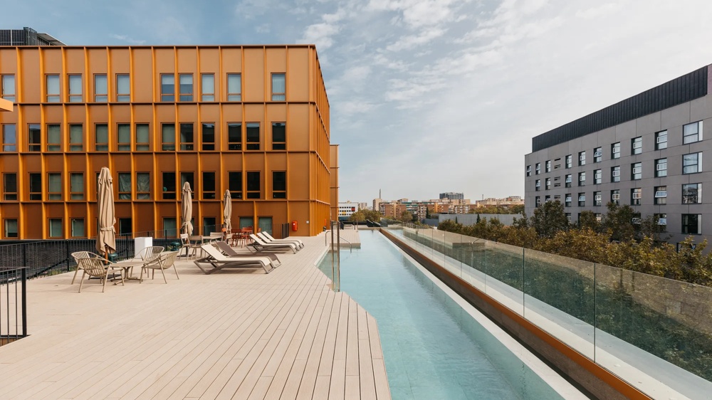 Roof terrace with sun loungers, parasols and pool next to a modern orange building.