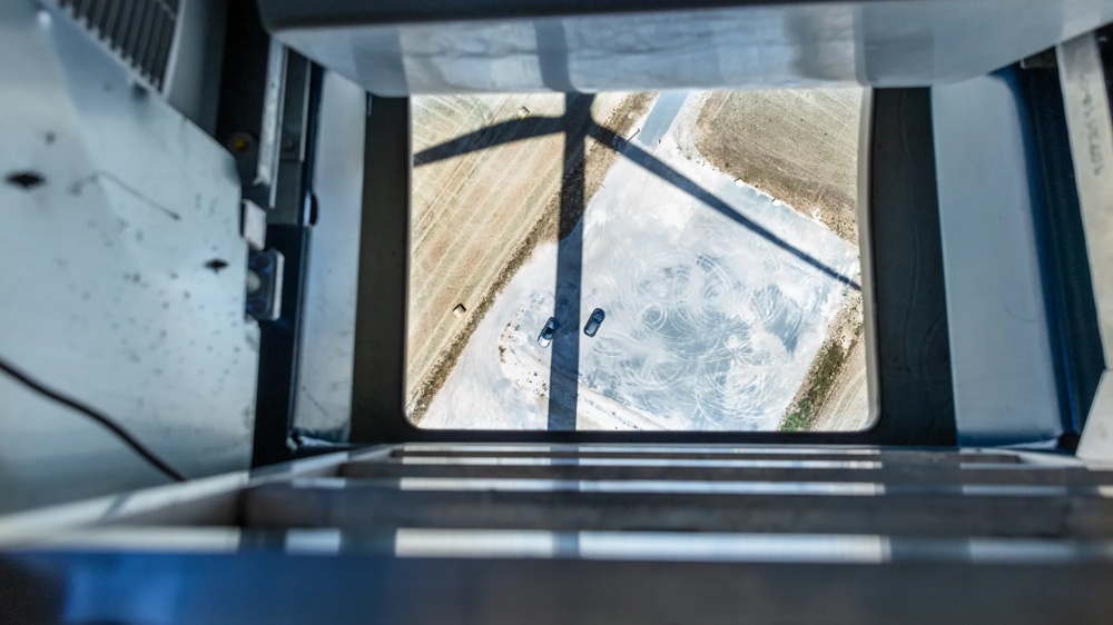 Eine Person steht auf einer Windkraftanlage und schaut auf ein Gerät, mit mehreren Windrädern im Hintergrund.