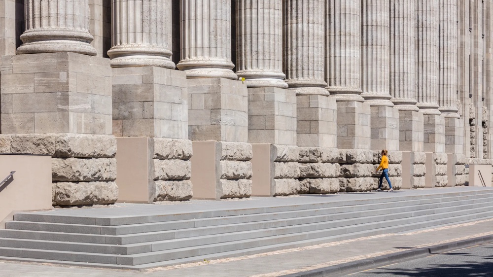 Eine Person in gelber Jacke geht vor großen Steinsäulen entlang.