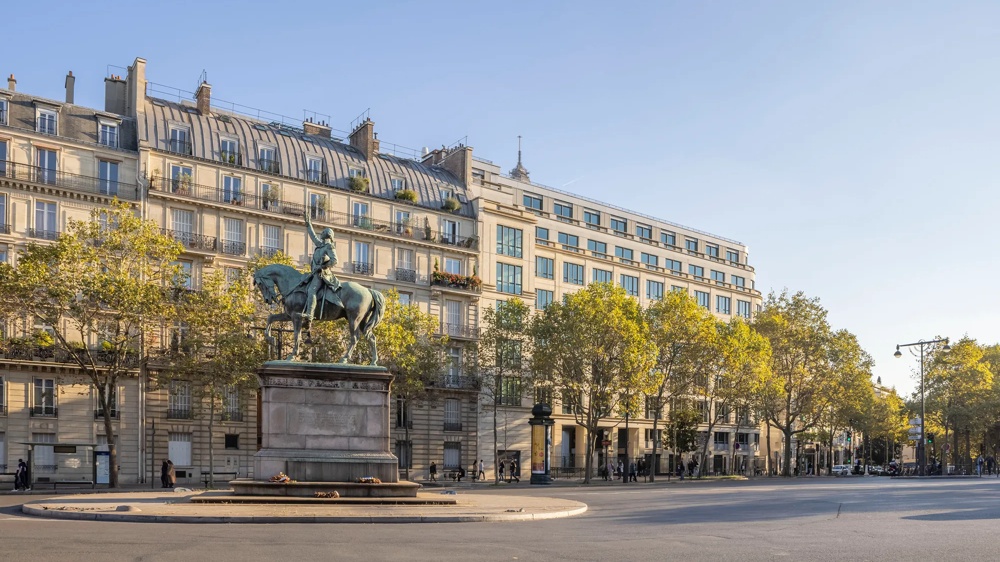 Reiterstatue auf einem Platz vor einem historischen Gebäude, umgeben von Bäumen.