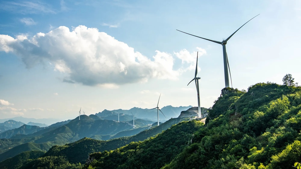 Windkraftanlagen auf bewaldeten Hügeln und Bergen unter blauem Himmel mit weißen Wolken