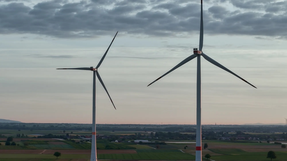 Weite grüne Felder mit mehreren Windturbinen unter einem bewölkten Himmel in der Ferne.