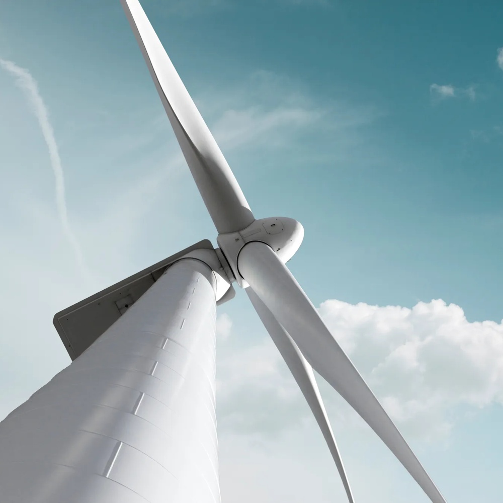 Nahaufnahme einer Windkraftanlage vor blauem Himmel mit weißen Wolken, Symbol für erneuerbare Energie