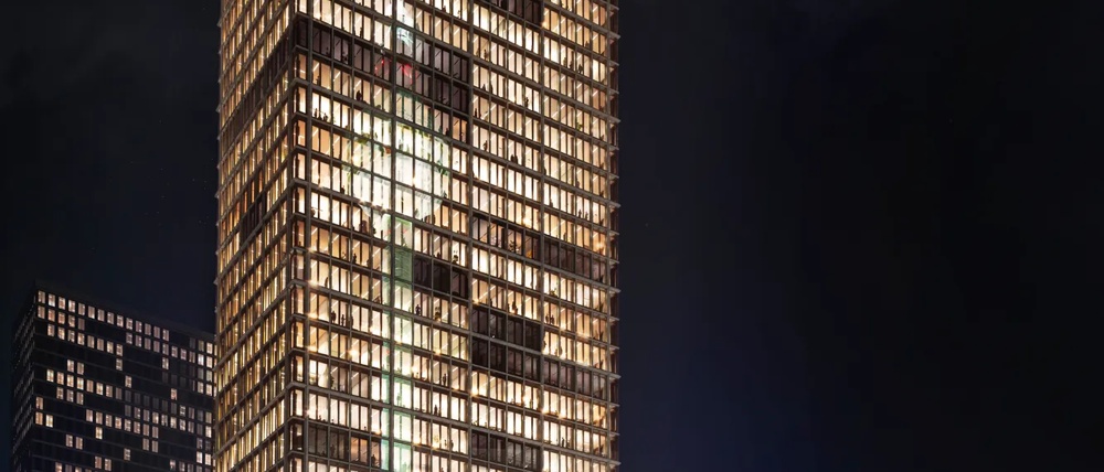 Beleuchtete Stadt bei Nacht, gelbe Straßenbahn zieht verwischte Linien vor modernen Glasgebäuden und Bahnhof.
