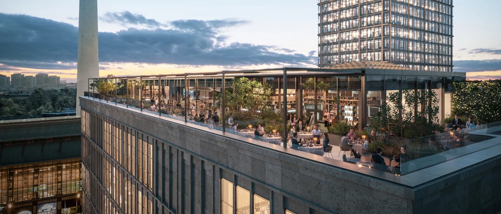 Ein Fernsehturm neben einem beleuchteten Hochhaus bei Sonnenuntergang, mit Terrasse im Vordergrund.