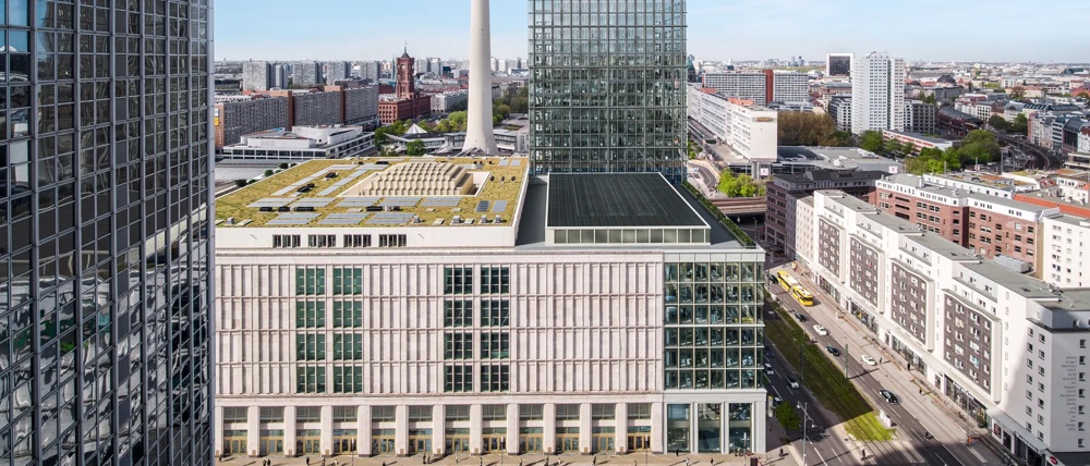 Moderne Hochhäuser und Fernsehturm überblicken eine belebte Stadtstraße bei klarem Himmel.