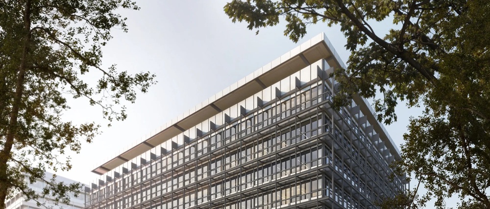 Ein modernes, verglastes Bürogebäude am Wasser, umgeben von Bäumen und Menschen auf einem Gehweg.