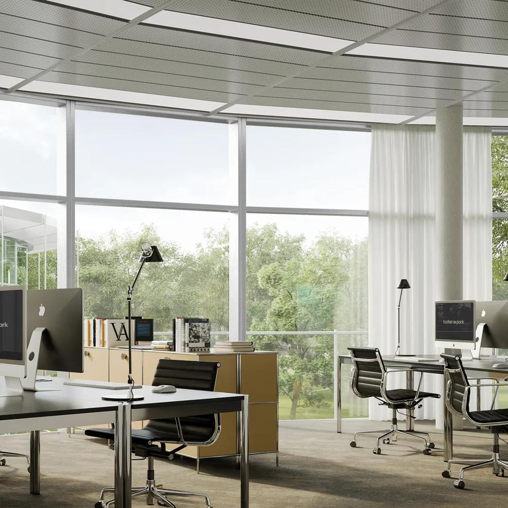 Modern office with large windows, several desks, computers and office chairs, surrounded by a green landscape.