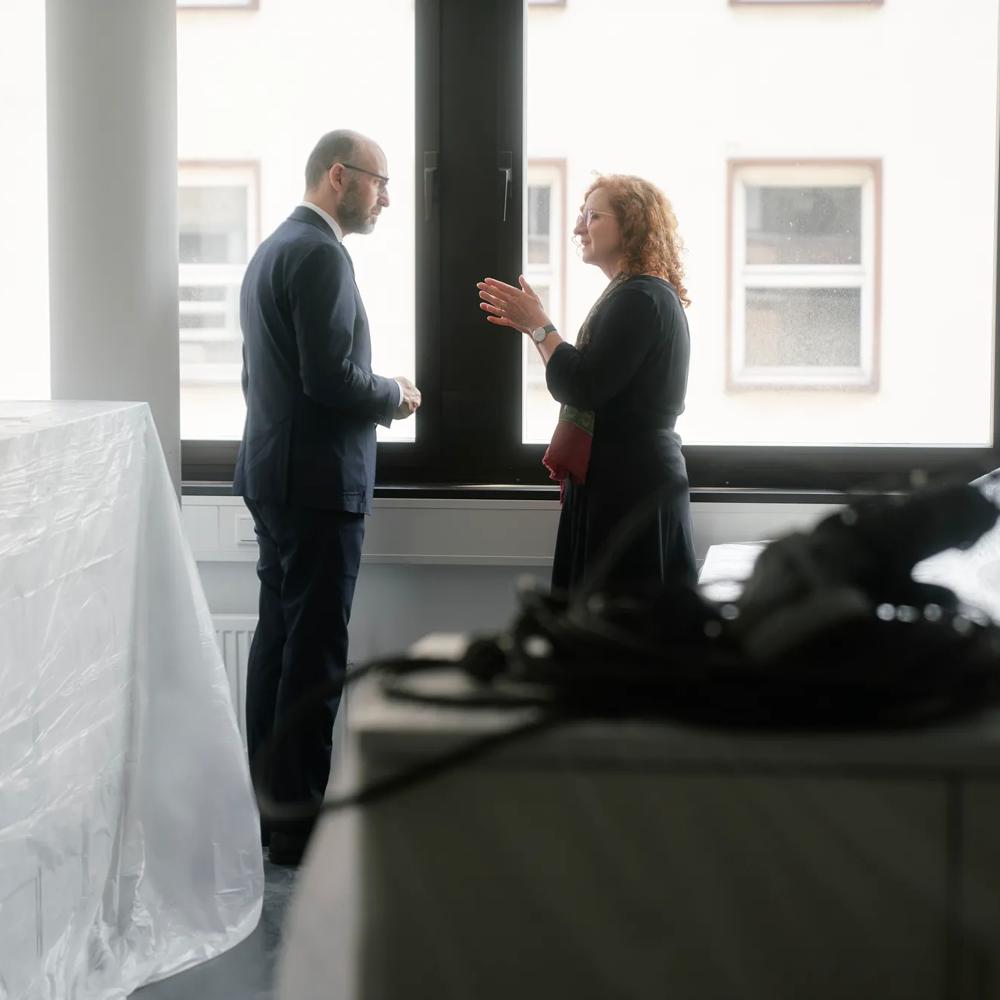 Ein Mann und eine Frau unterhalten sich vor einem großen Fenster in einem Büro.