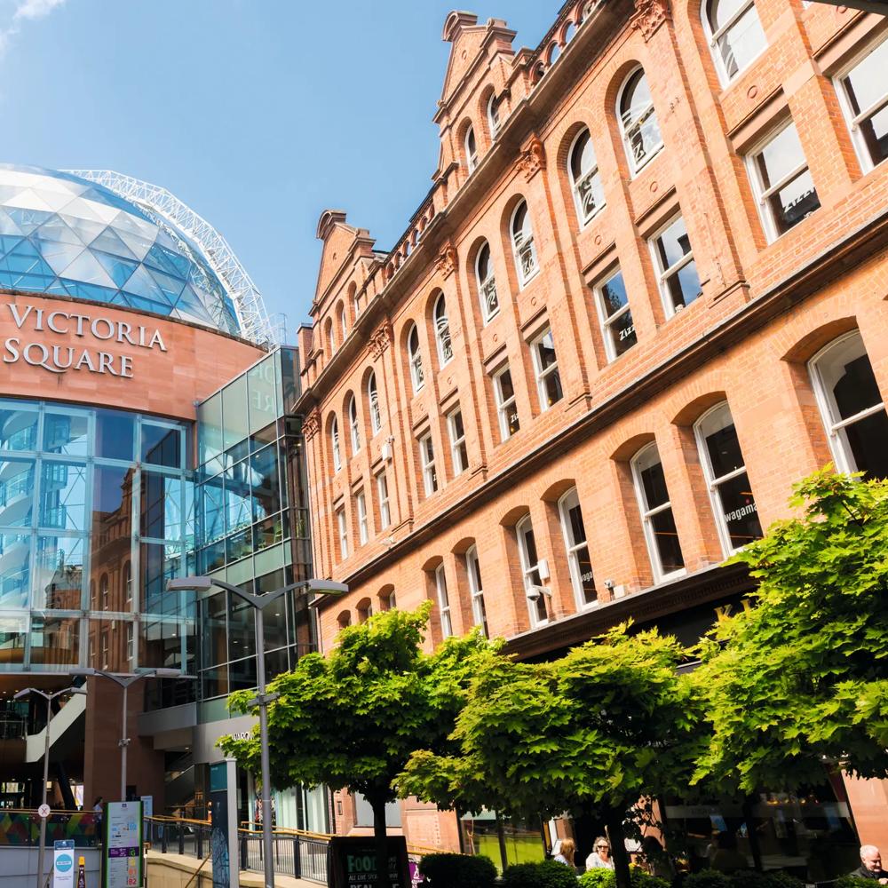 Einkaufszentrum Victoria Square mit gläserner Kuppel, flankiert von roten Backsteingebäuden und Bäumen.