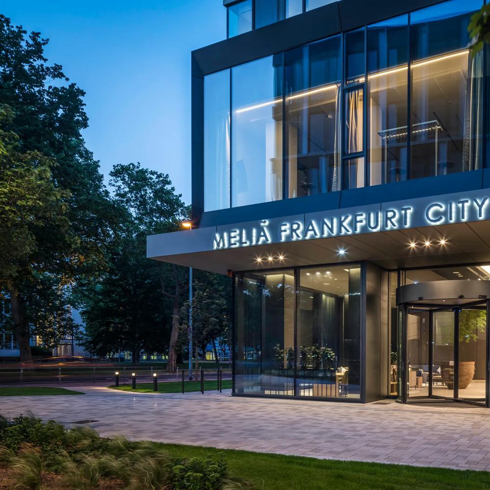 Eingang des Melia Frankfurt City Hotels bei Dämmerung, mit Glasfront und beleuchtetem Schriftzug.