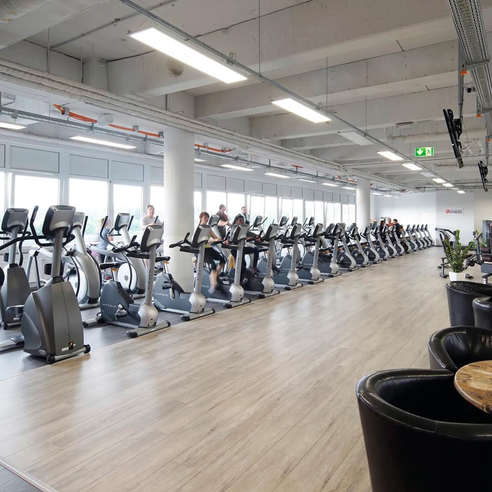 Reihe von Fitnessgeräten in einem hellen Fitnessstudio, Menschen trainieren auf Crosstrainern.