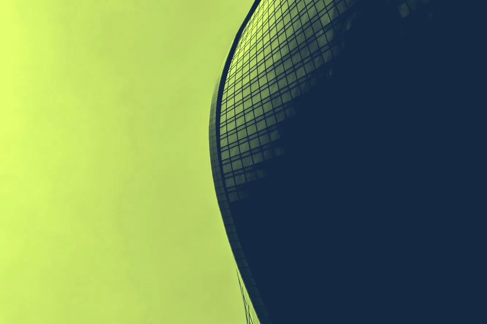 Gebogenes Hochhaus mit Glasfassade vor grünem Himmel.