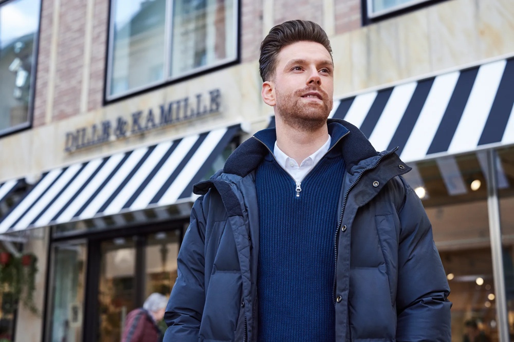 Ein Mann in blauer Jacke steht vor einem Geschäft mit schwarz-weiß gestreifter Markise.