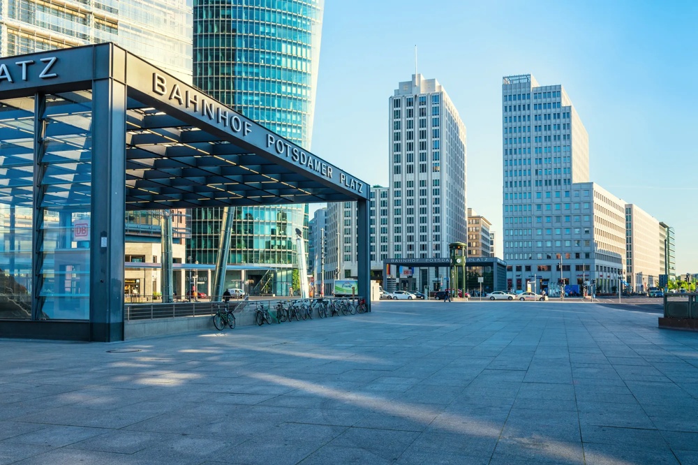 Eingang zum Bahnhof Potsdamer Platz, umgeben von modernen Hochhäusern unter klarem blauem Himmel.