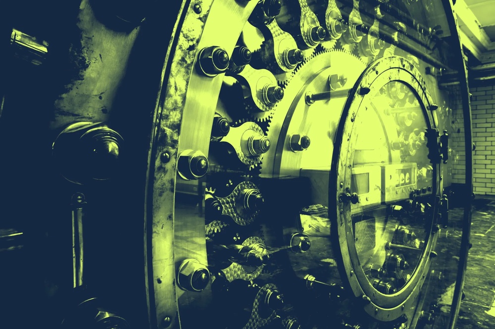 Ein massives, rundes Stahltresortor mit Zahnrädern und Bolzen, in grünlichem Licht beleuchtet.