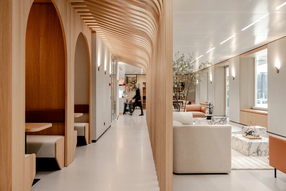 Moderner Innenraum mit Holzverkleidung, Sitznischen und Pflanzen, eine Person geht durch den Flur.