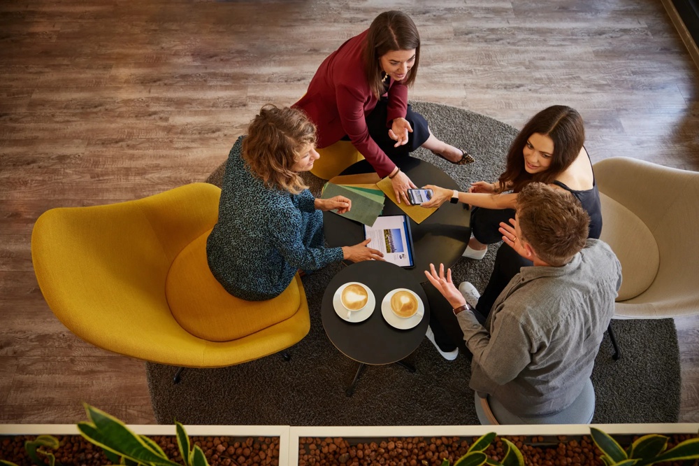 Four people are sitting around a table with coffee and documents while discussing.