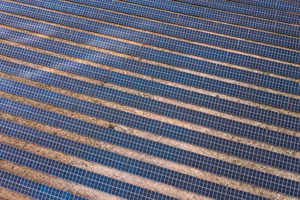Reihen von blauen Solarpaneelen auf braunem Erdboden in schräger Anordnung.