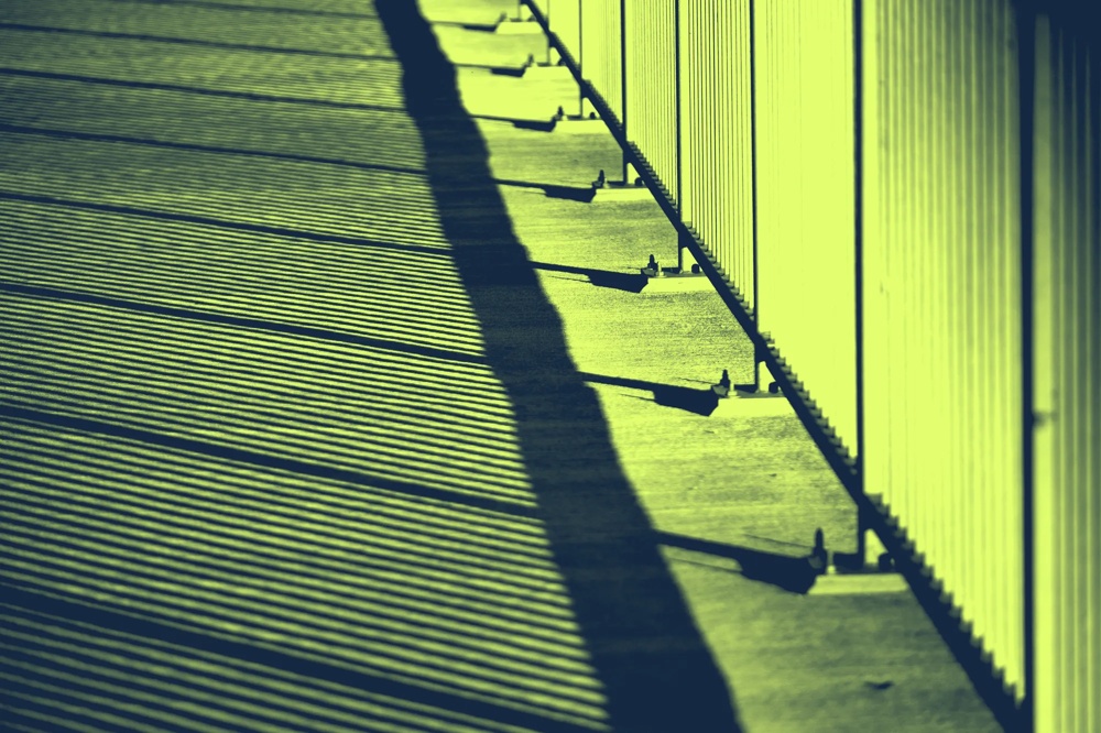 Schatten von Geländerstäben werfen parallele Linien auf einen Gehweg in gelbem Licht.