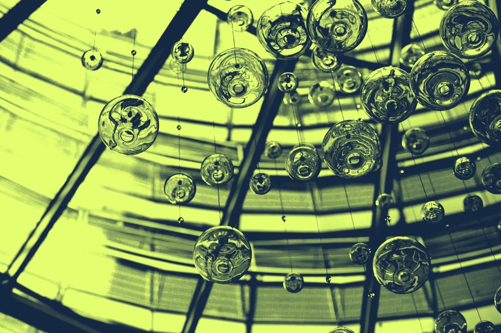 Glasblasen hängen an Fäden vor einem geometrischen, grün getönten Dachfenster.