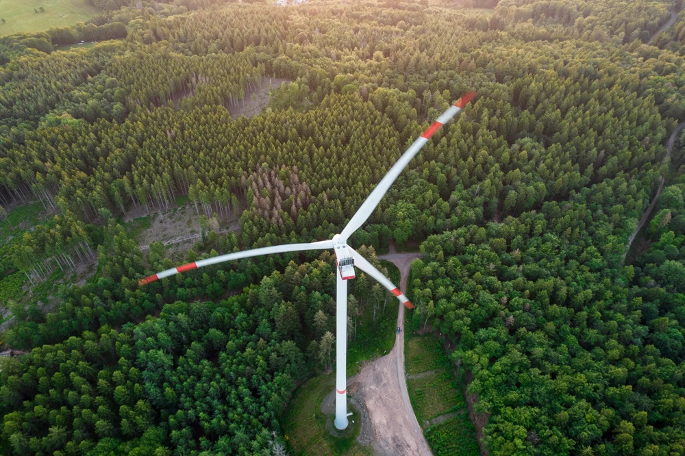 Eine Windkraftanlage steht inmitten eines dichten Waldes aus der Vogelperspektive.