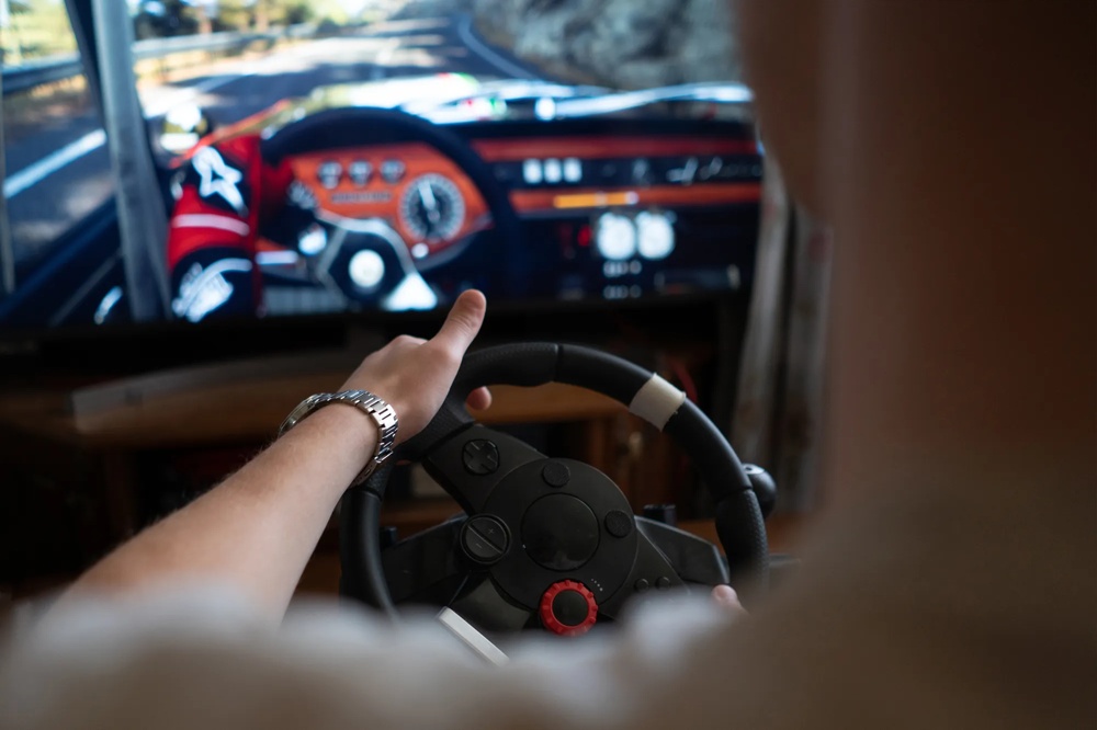 Person spielt in einem Fahrsimulator ein Autorennspiel mit Lenkrad vor einem Bildschirm.