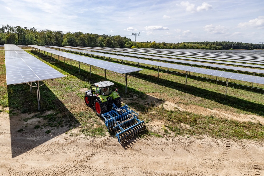 Landwirtschaftliche Maschine arbeitet zwischen Reihen von Solarmodulen.
