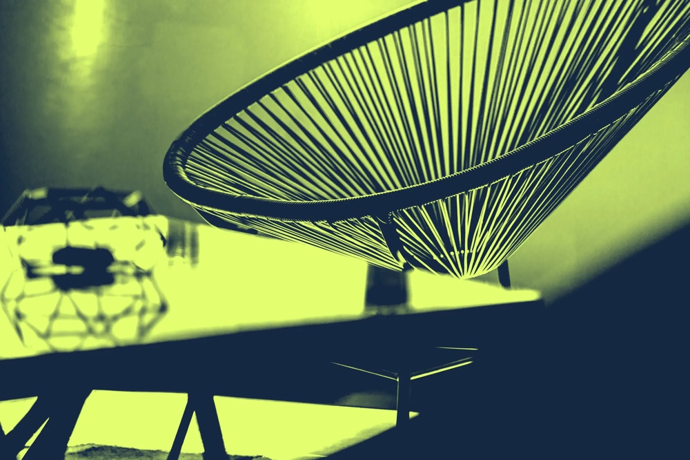 Ein moderner Stuhl mit Drahtgeflecht neben einem geometrischen Objekt auf einem Tisch.