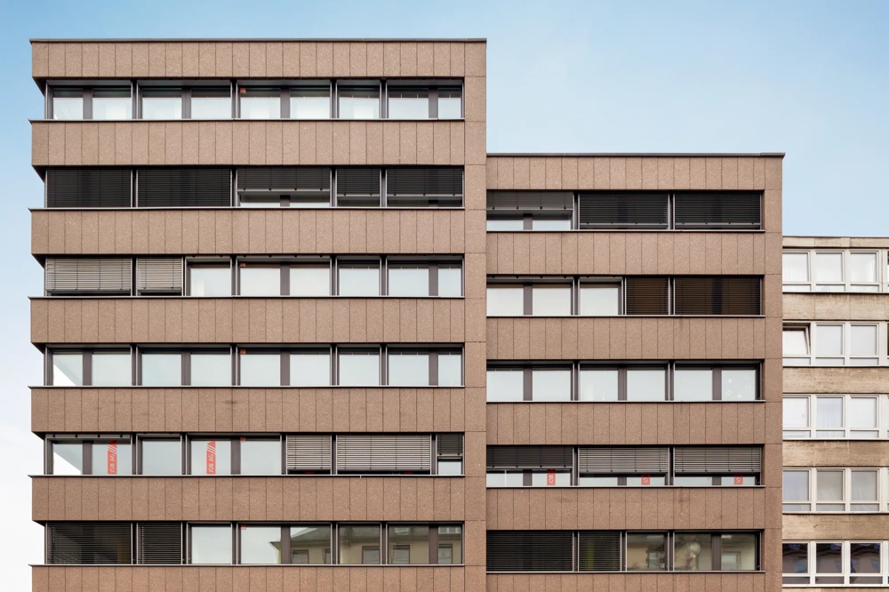 Brown, modern building with several floors and windows, blue sky in the background.