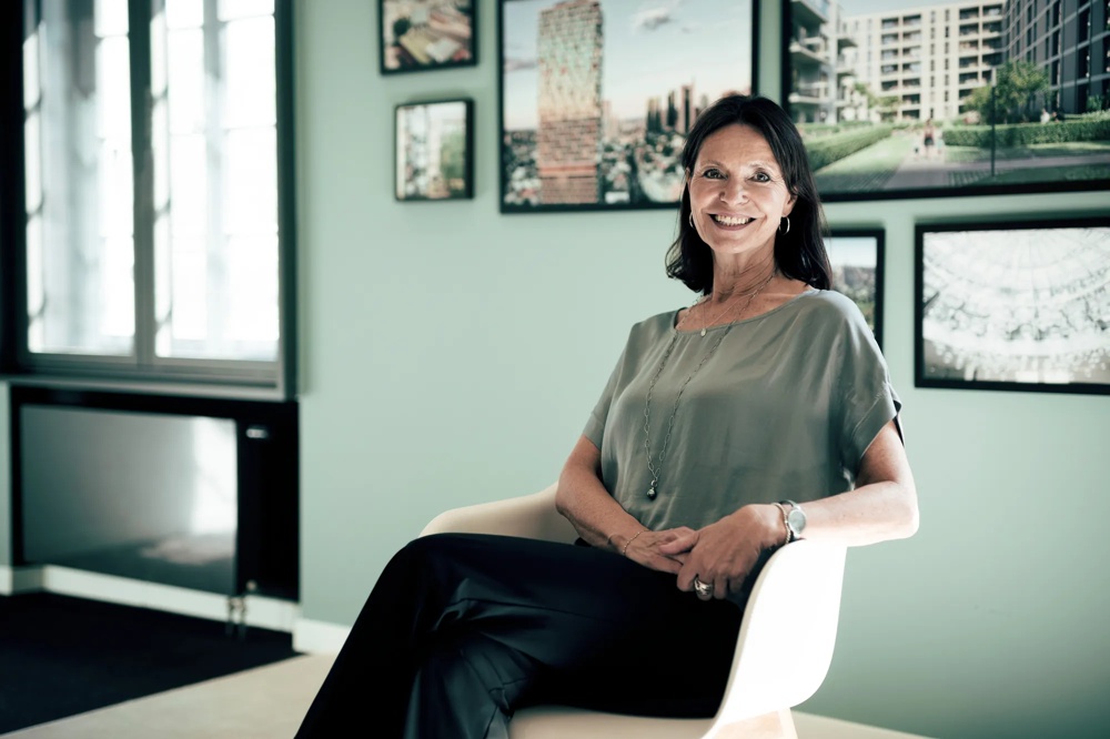 Woman sitting smiling on chair in front of mint green wall with framed pictures.