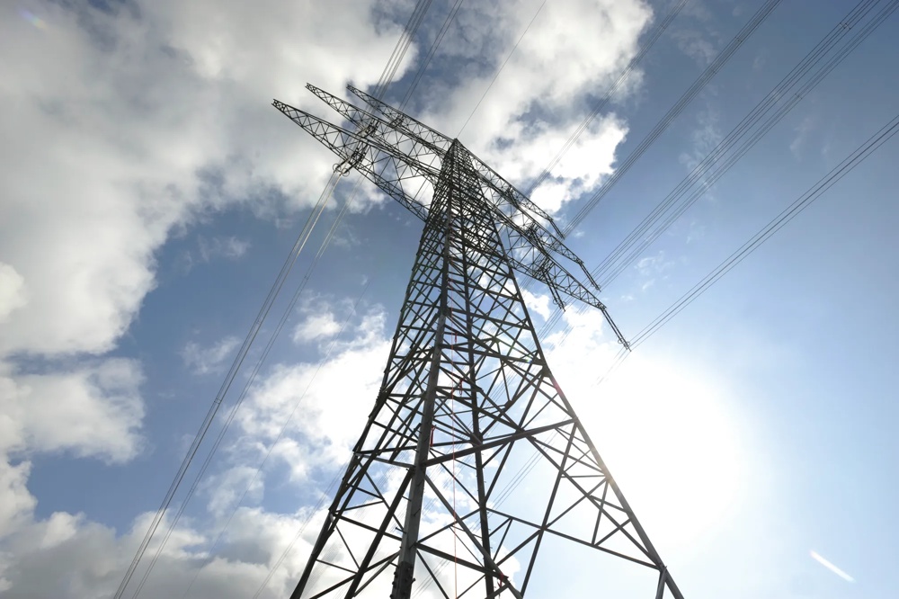 Ein Strommast ragt in den blauen Himmel, umgeben von weißen Wolken.