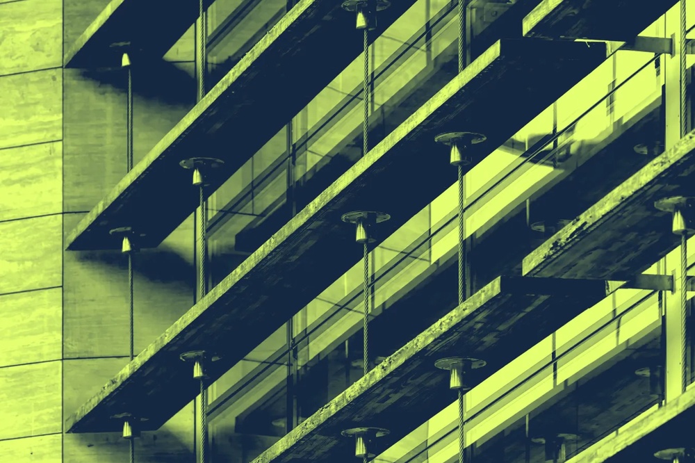 Schräge Ansicht eines modernen Gebäudes mit Glasbalkonen und vertikalen Linien in grünlichem Farbton.