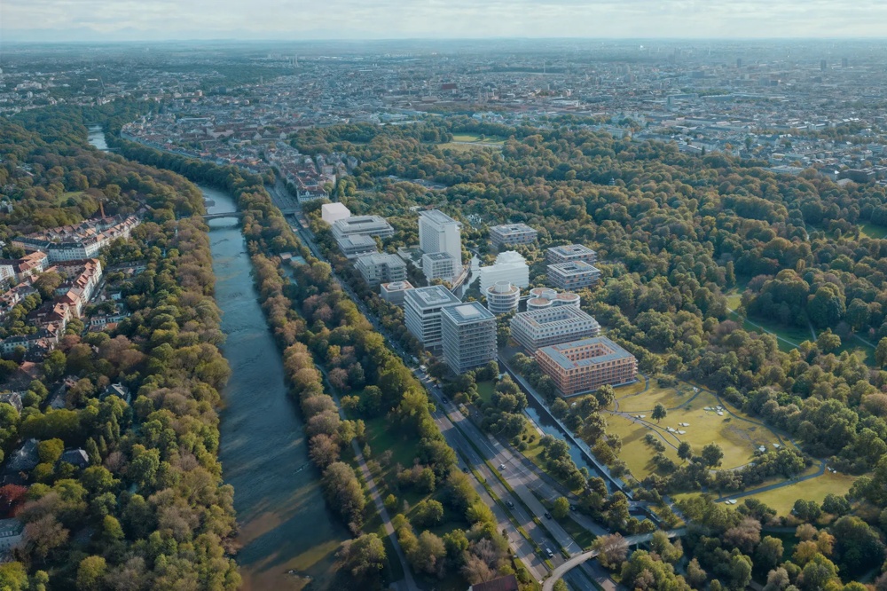 Luftaufnahme einer Stadt mit Fluss, umgeben von Bäumen und modernen Gebäuden, bei klarem Himmel.