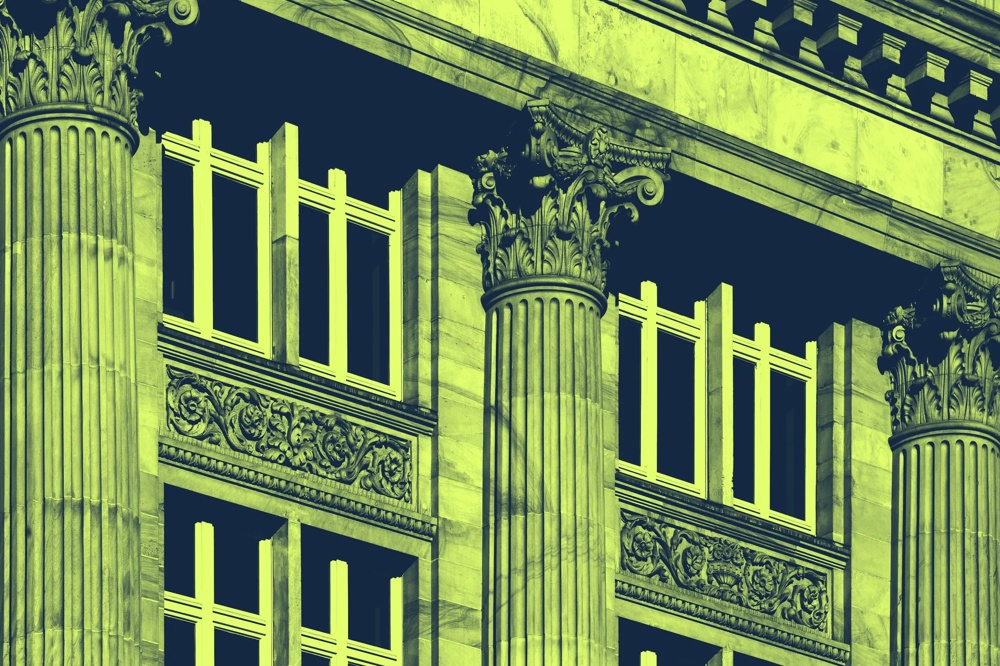 Verzierte Steinsäulen und Fenster eines historischen Gebäudes in grünlich-gelbem Farbton.