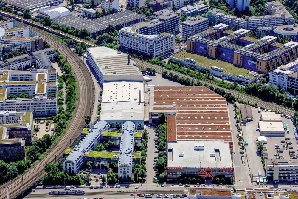Aerial shot of an urban area with buildings, roads and railway tracks surrounded by green spaces.
