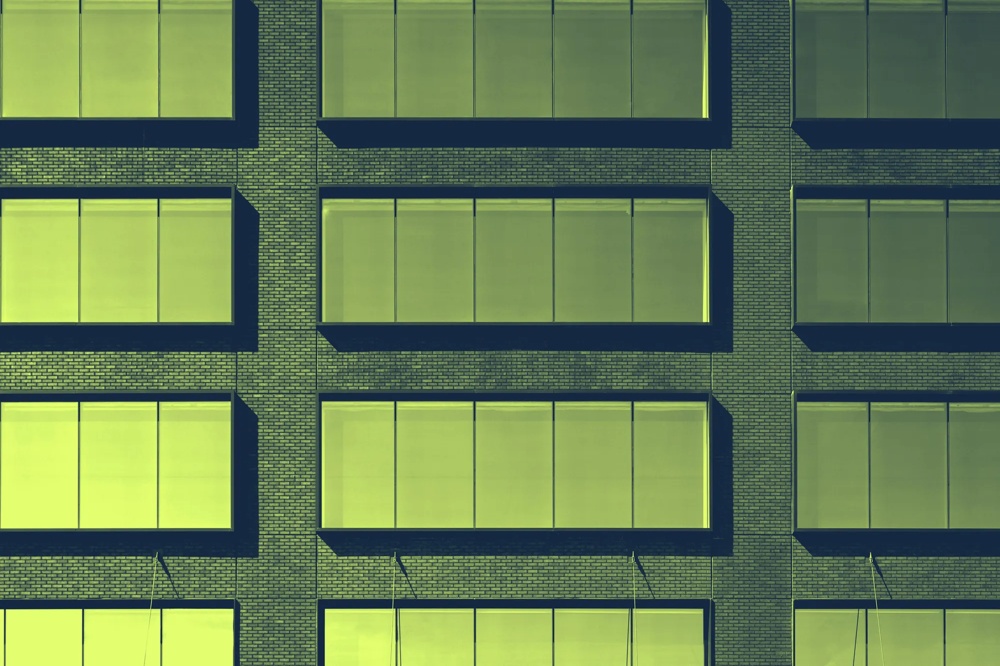 Fassade eines Gebäudes mit großen, gelb getönten Fenstern in gleichmäßigen Reihen auf Backsteinmauer.