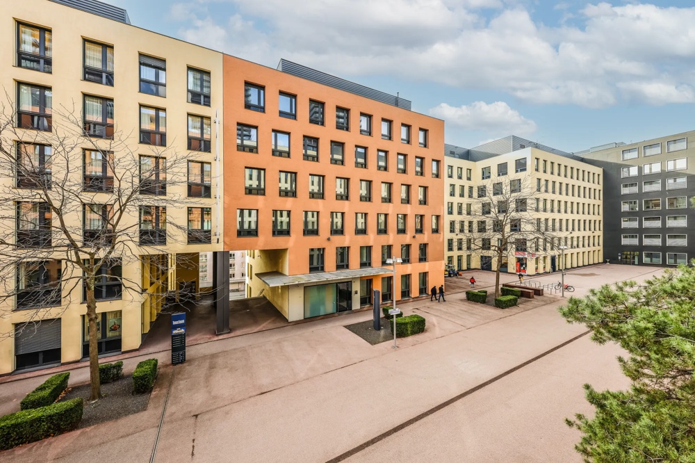 Mehrere moderne Bürogebäude mit bunten Fassaden und kahlen Bäumen an einem bewölkten Tag.