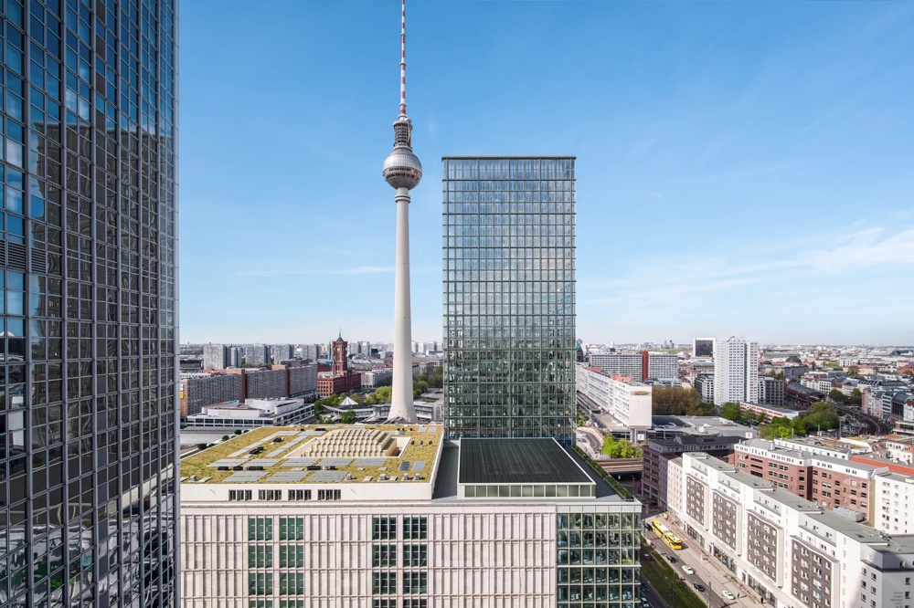 Moderne Hochhäuser und Fernsehturm überblicken eine belebte Stadtstraße bei klarem Himmel.