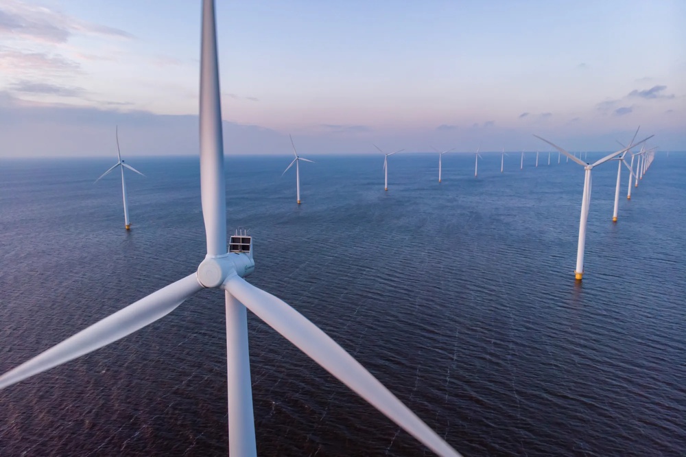 Offshore wind farm at sunset, with several wind turbines in a row over calm water.