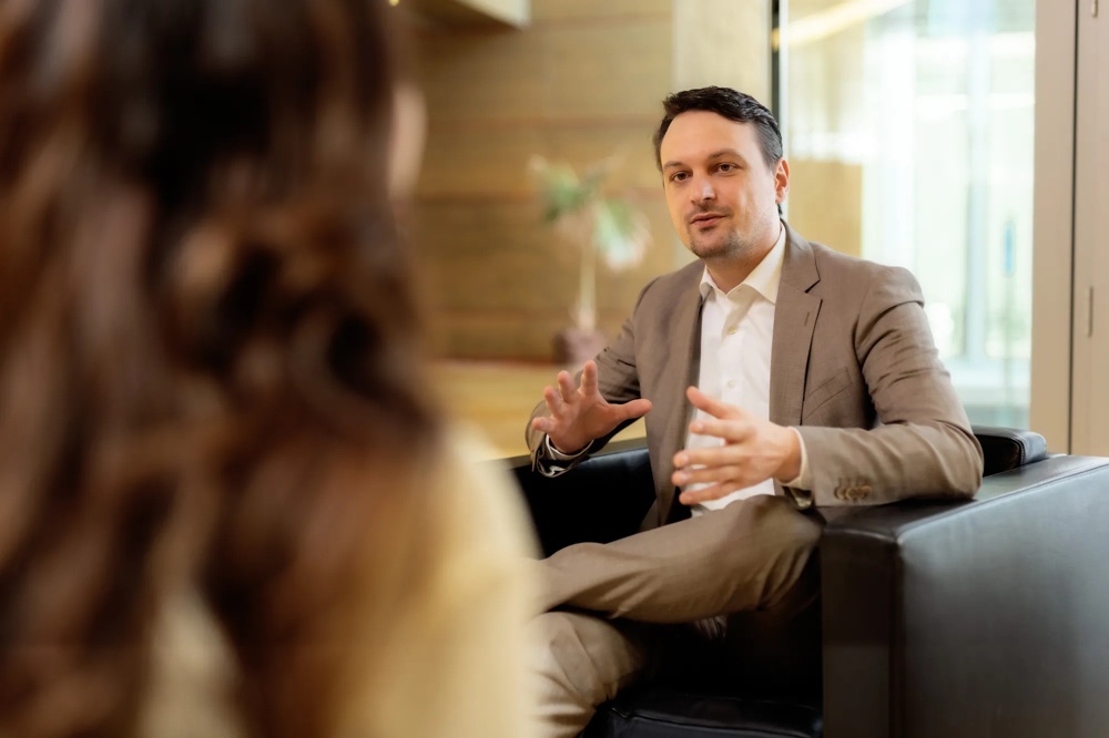 A man in a suit talking gesticulatingly to a blurry person in a modern office.