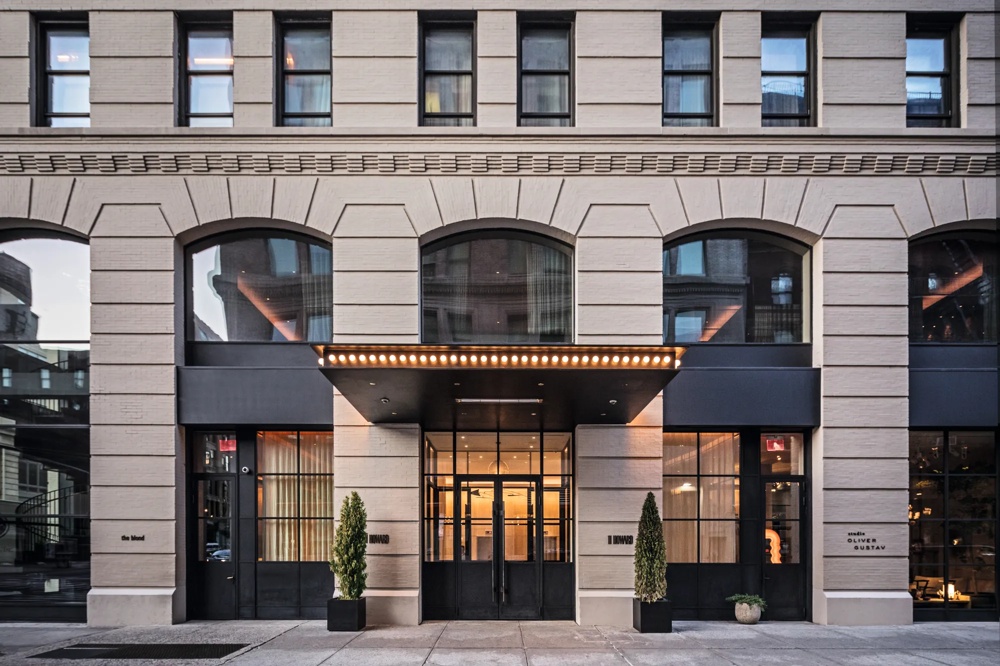 Eingang eines modernen Gebäudes mit großen Fenstern und zwei Pflanzen in schwarzen Töpfen.