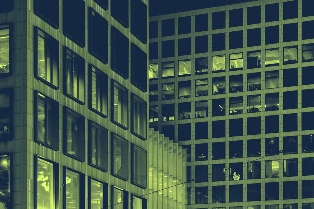 Moderne Gebäude mit vielen erleuchteten Fenstern bei Nacht, geometrische Strukturen und rechteckige Muster.