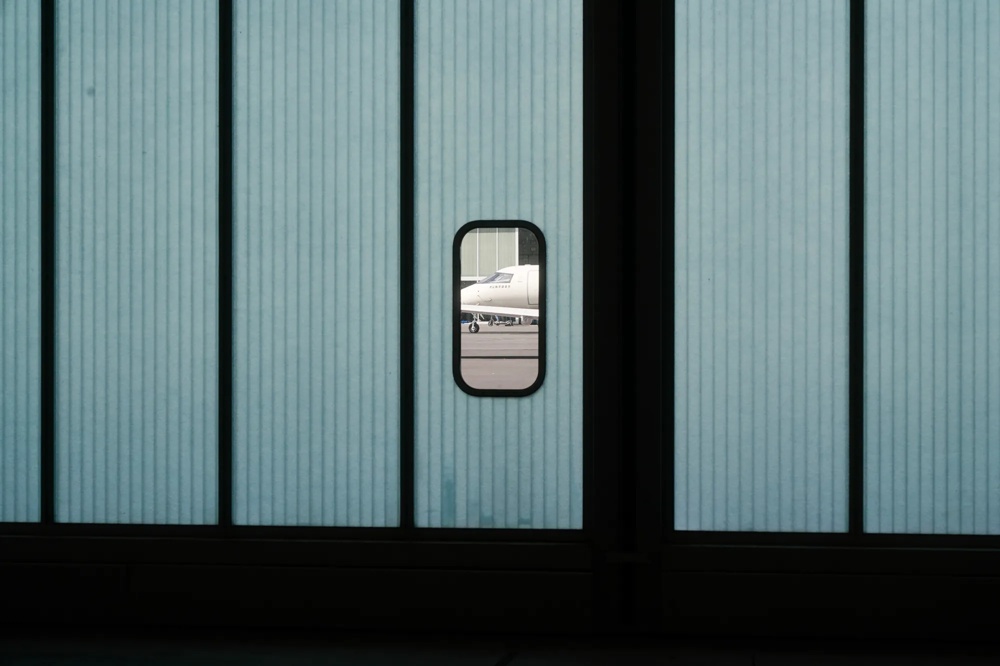 An aeroplane can be seen through a small window in a large ribbed hangar door.