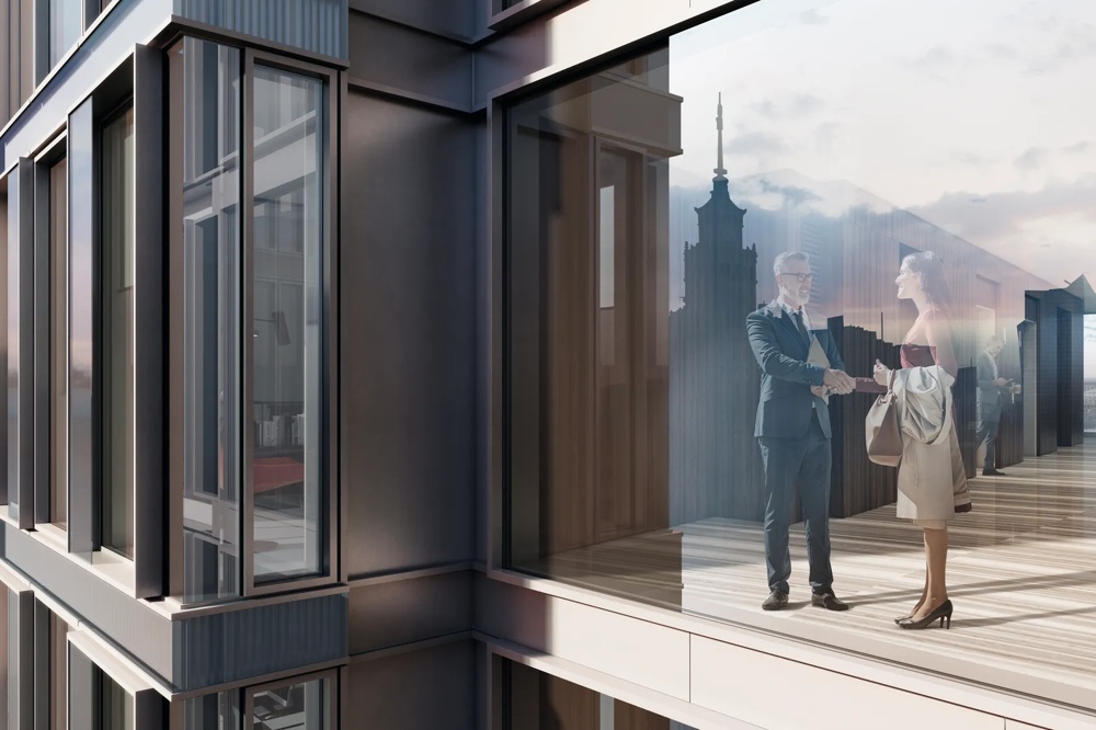 Two people shaking hands in a modern office building with a glass facade, city view in the background.