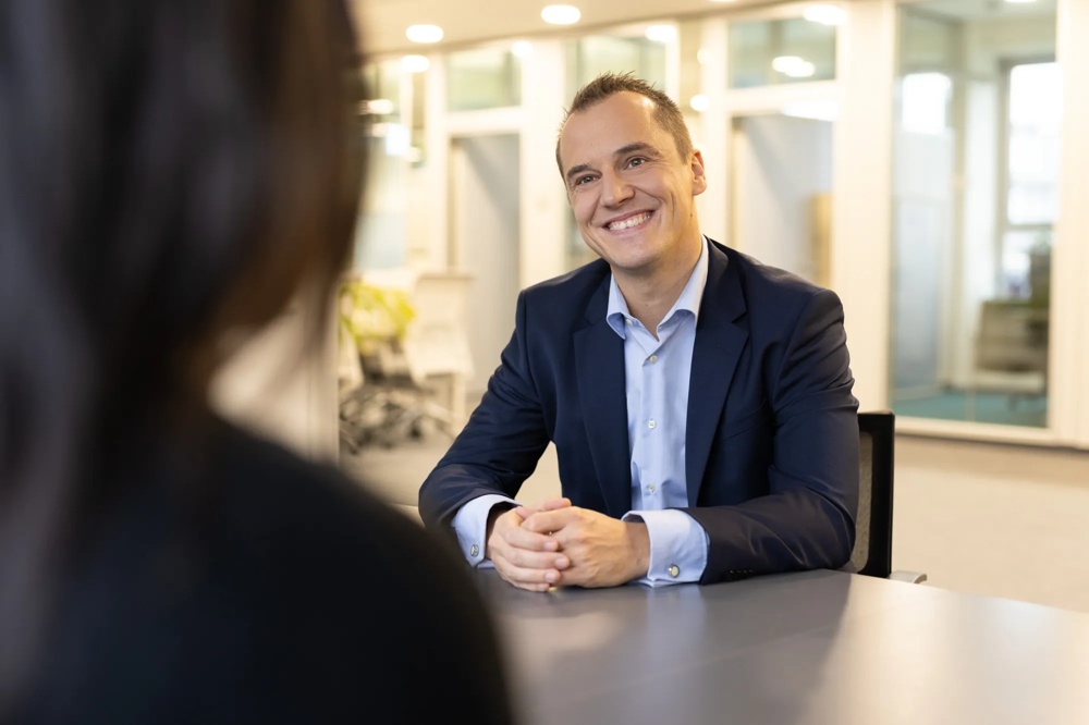 A man in suit smiling at a table in a modern office.