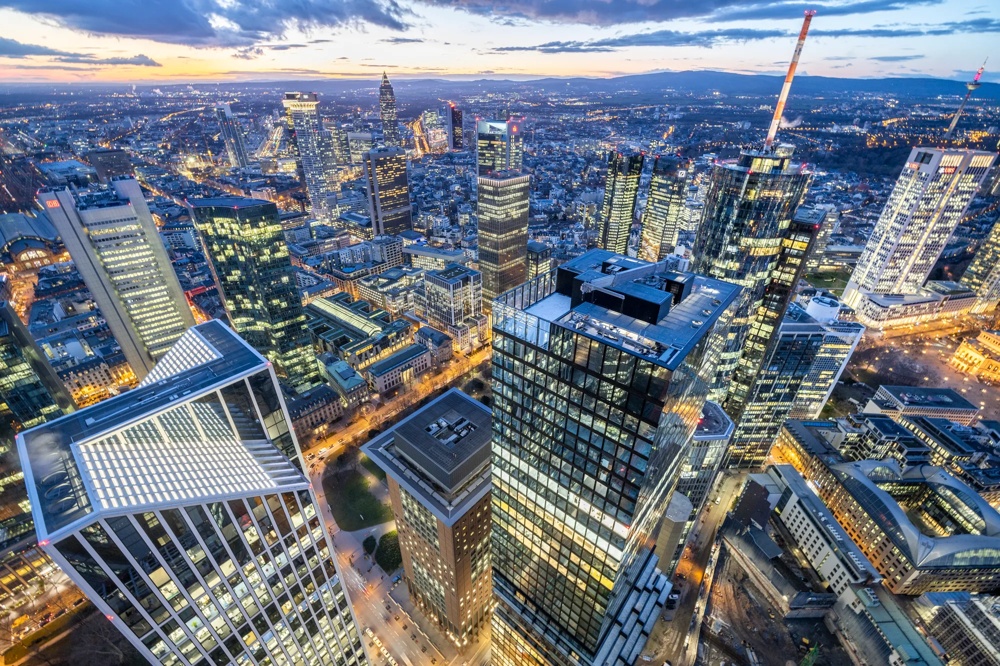 Blick auf eine beleuchtete Skyline einer Stadt bei Dämmerung mit vielen Hochhäusern und Straßen.