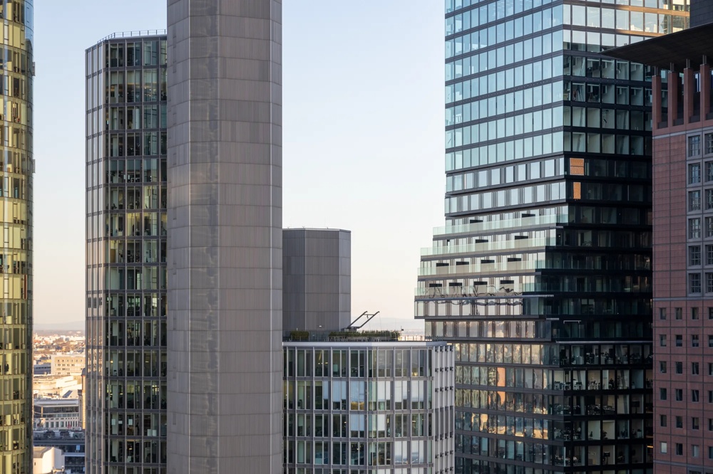 Mehrere moderne Hochhäuser mit Glasfassaden bei Tageslicht, blauer Himmel im Hintergrund.